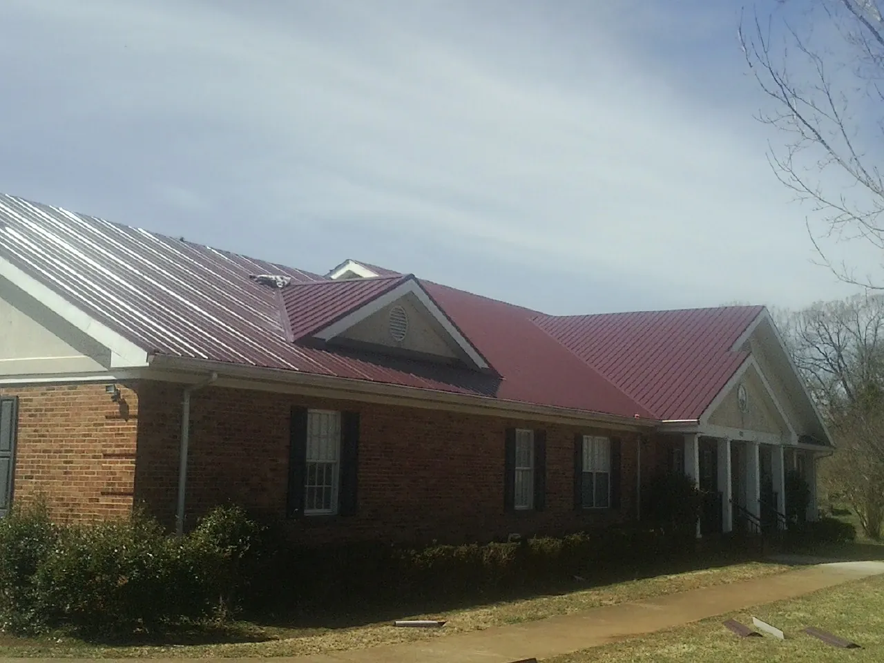 Red metal roof with gabled entries on a long brick building, from a Hail Damage Roof Repair job in Davenport